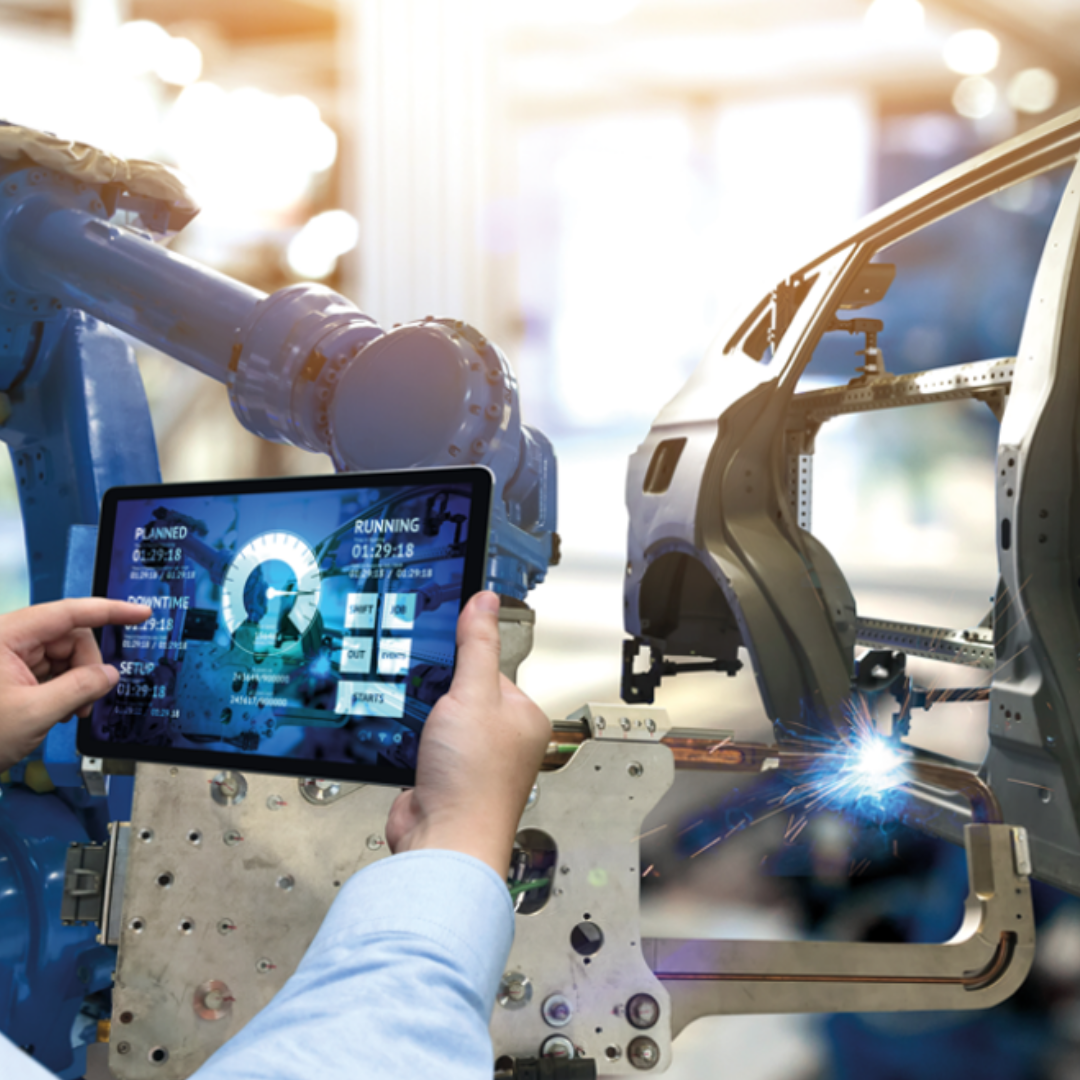 Car production line robotic machinery in the background and two hands holding and navigation an iPad in the foreground