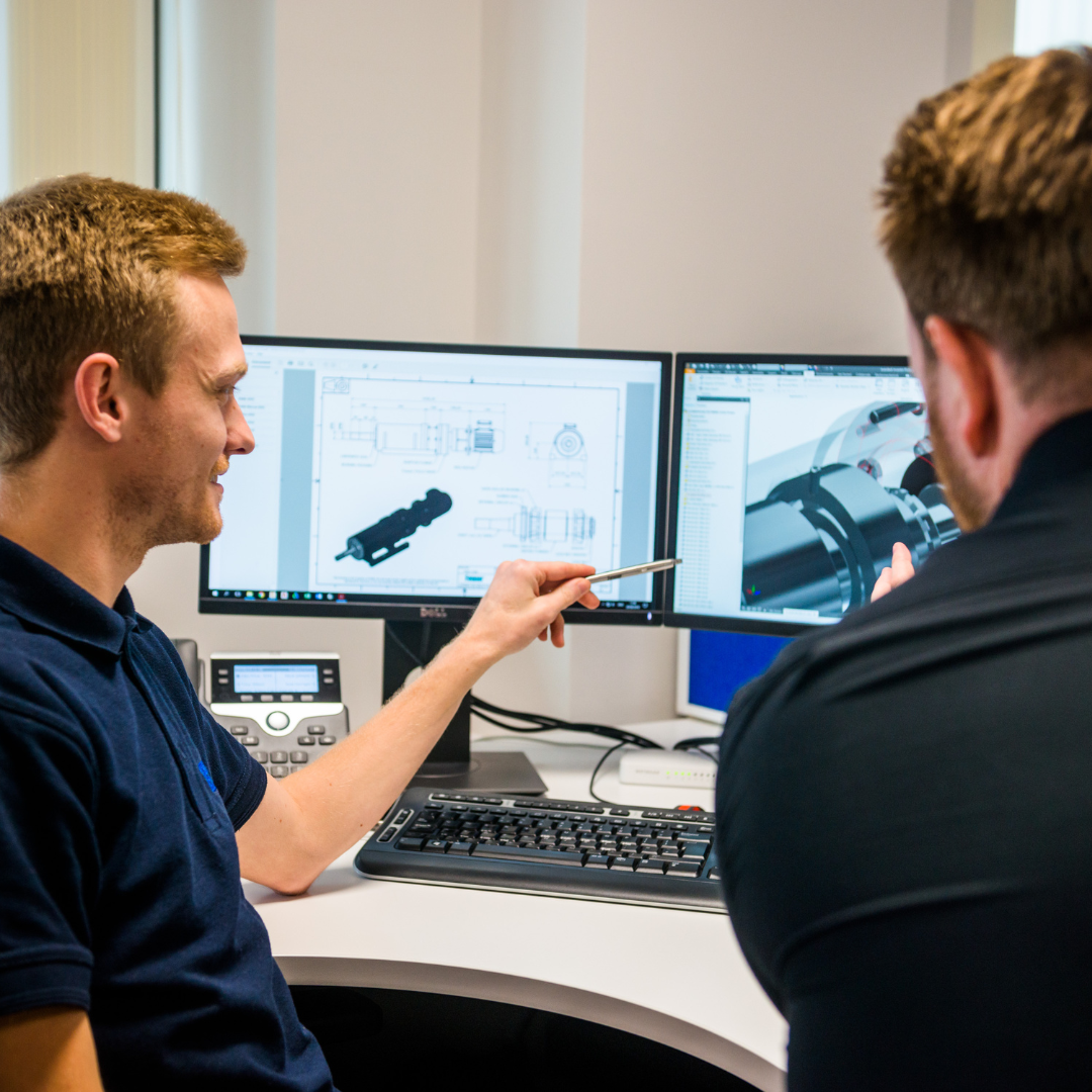 Two males view data on two screens in an office