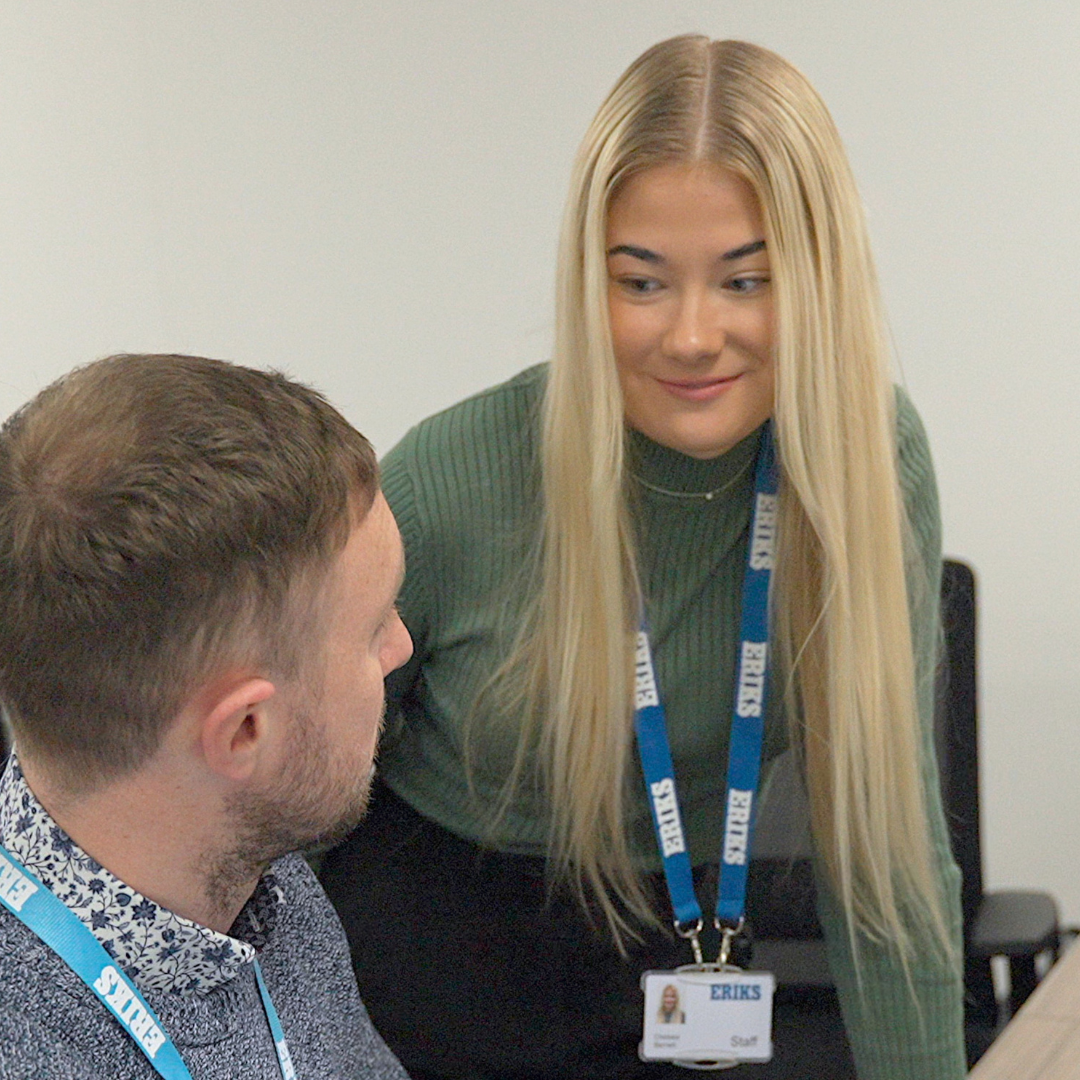 A woman looking at a male colleague sitting both smiling in an office setting