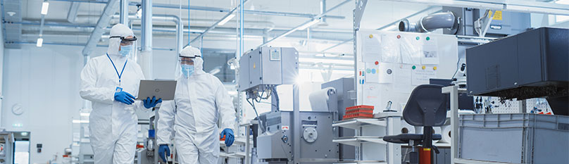 Bio-Pharma workers in a white and steel clean area, working on a laptop, for manufacturing medicine 