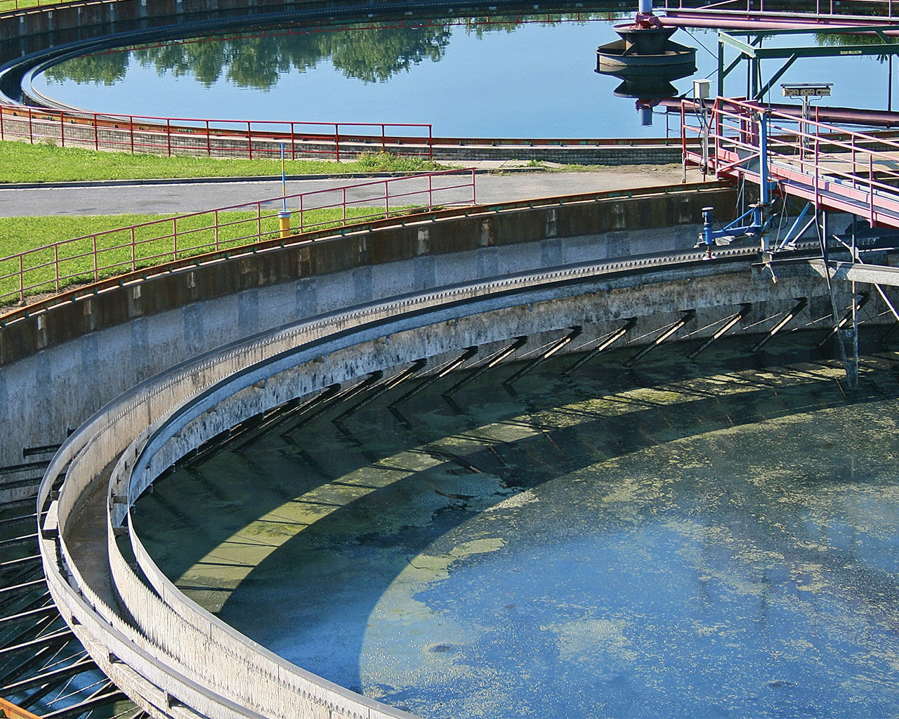 Close up of a large waste water cylinder, outside, with a small bridge over the water for treatment plant engineers