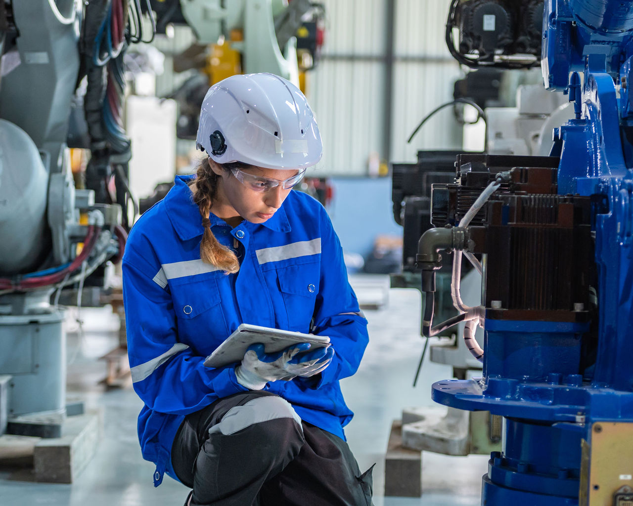woman engineer in uniform helmet inspection check control heavy machine robot arm construction installation in industrial factory. technician worker check for repair maintenance electronic operation