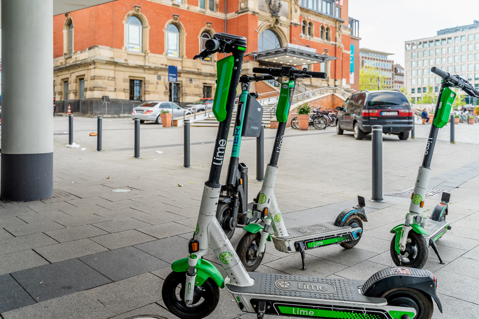 electric scooters from the rental company Lime are parked at the entrance of a hotel at the main station - modern green transport for rent e-scooter