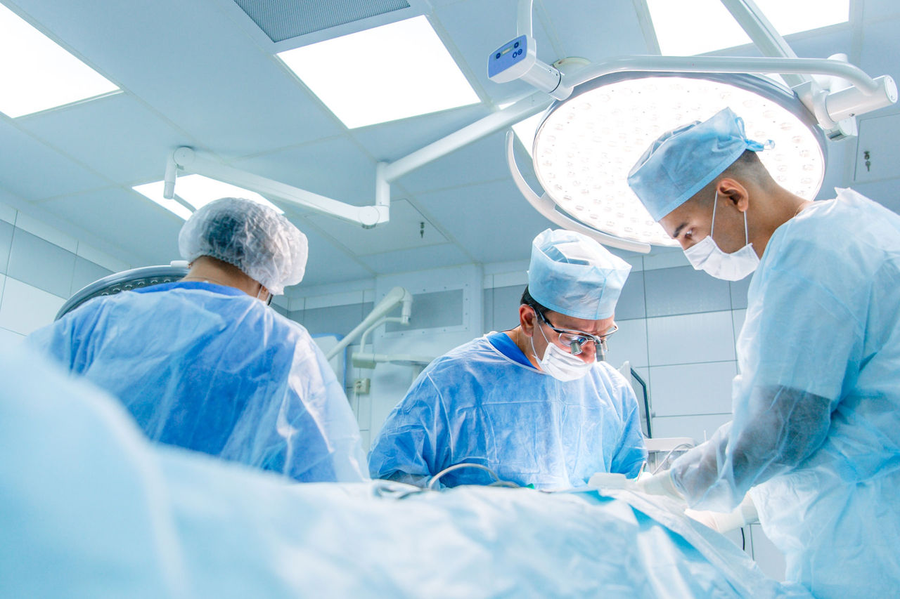 Surgeons in binocular lenses operate the patient lying under anesthesia in the operating room