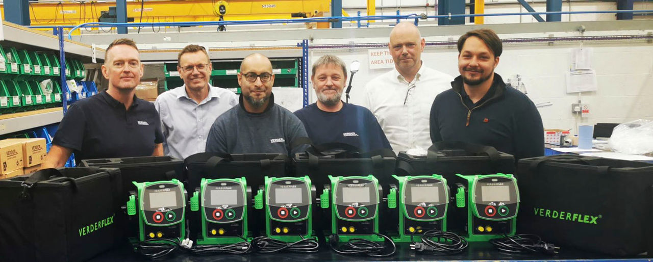 group of 6 men who are the Verderflex team standing behind a row of 6 Verderflex Ds500 pumps