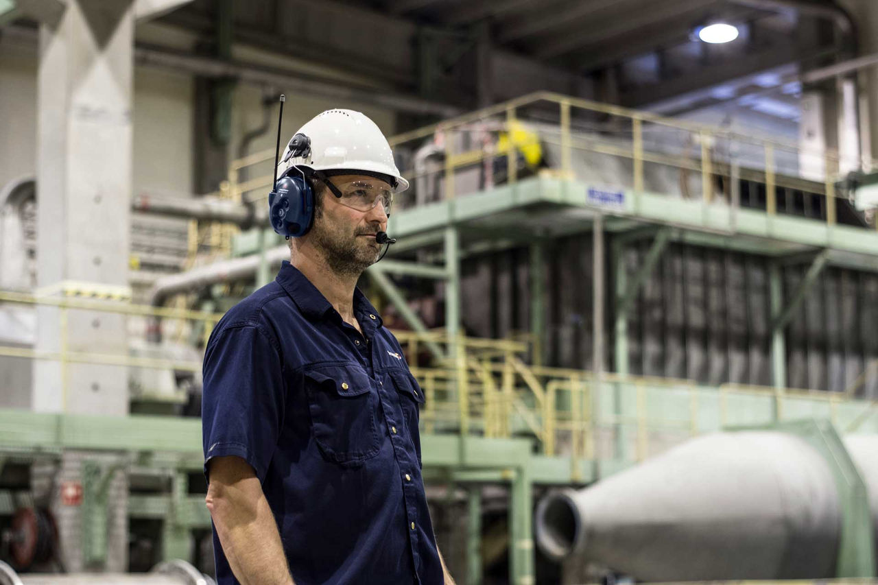 man in factory wearing white 3M helmet with attached Bluetooth headphones for communication