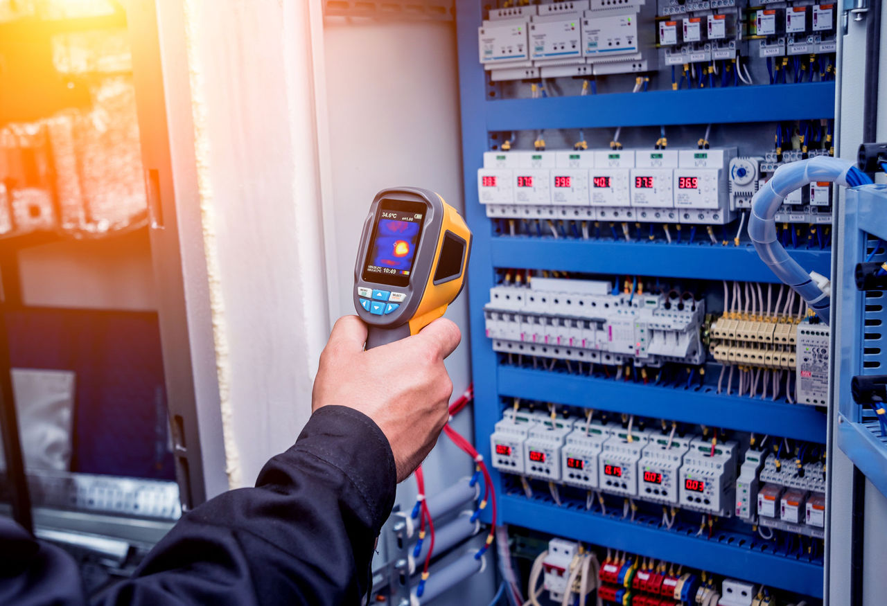 Turning up the heat on electrical efficiency Technician use infrared thermal imaging camera to check temperature at fuse-box