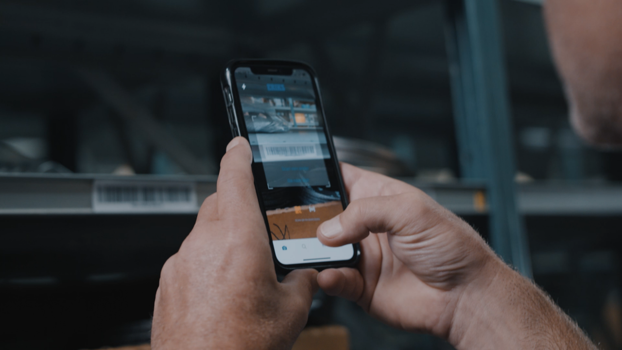 Warehouse setting with a person's hand holding a phone scanning a barcode label on a shelf holding products