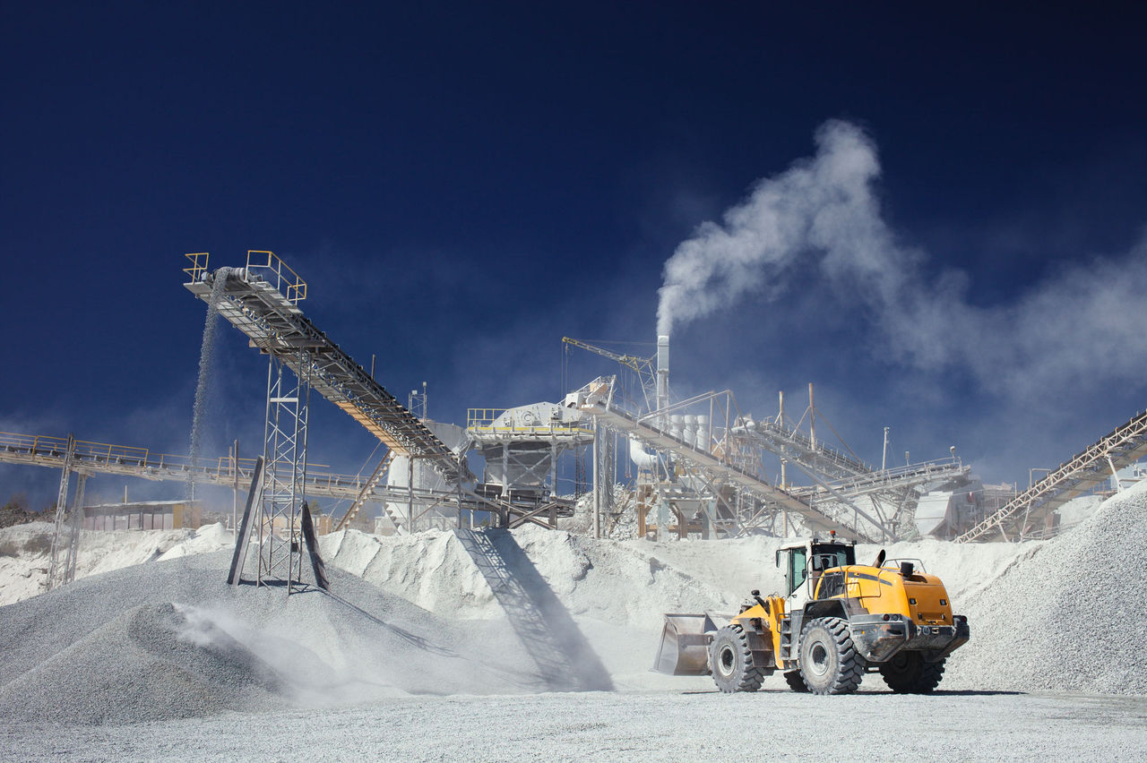 2183570091 Huge quarry with vans and trucks in a dramatic background and dusty extraction on conveyor carrying huge rocks